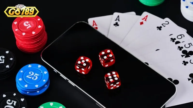 Nạp Tiền GO789 Qua Ngân Hàng, Ví Điện Tử Và Thẻ Cào 3 Chip casino, xúc xắc đỏ và bộ bài đặt cạnh điện thoại có logo GO789